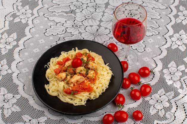 vista dall'alto pasta gialla cotta con ali di pollo e salsa di pomodoro all'interno della banda nera sul tavolo coperto bianco