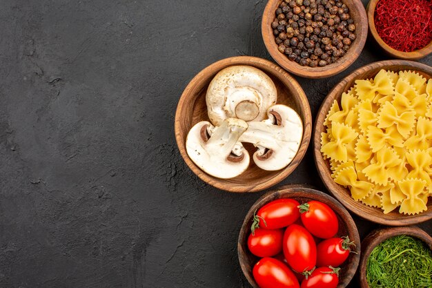 Vista dall'alto pasta italiana cruda con condimenti e funghi sulla scrivania scura