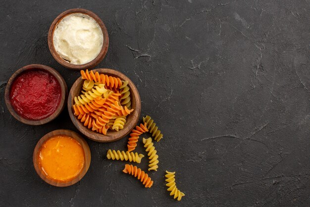 Vista dall'alto pasta italiana cruda pasta a spirale insolita con condimenti su oscurità