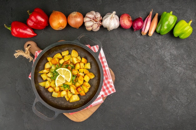 Vista dall'alto patate fritte all'interno di una padella con limone e verdure su sfondo scuro