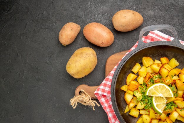 Vista dall'alto patate fritte all'interno di una padella con limone sullo sfondo scuro