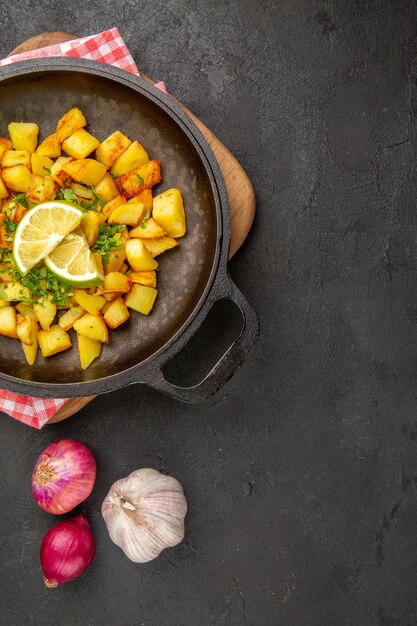 Vista dall'alto patate fritte all'interno di una padella con limone sullo sfondo scuro