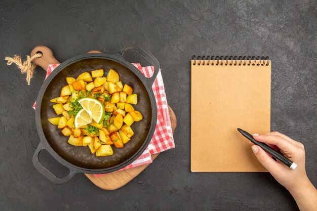 Vista dall'alto patate fritte all'interno di una padella con verdure e limone sul pavimento scuro cucina alimentare color pepper