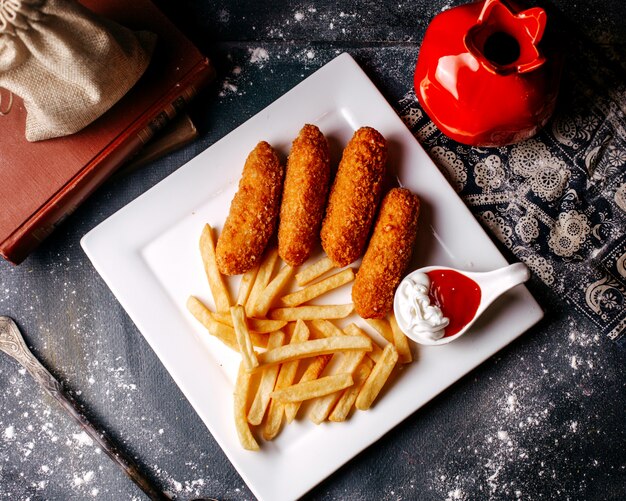 Vista dall'alto patatine fritte con patatine fritte all'interno del piatto bianco e con ketchup e maionese sul pavimento grigio