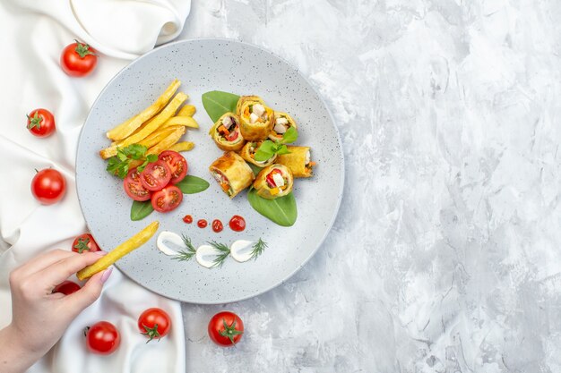 Vista dall'alto patè di verdure rotoli con pomodori e patatine fritte all'interno della piastra sulla superficie bianca