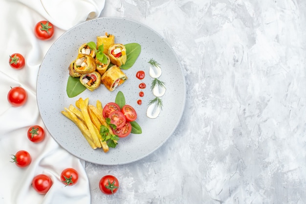 Vista dall'alto patè di verdure rotoli con pomodori e patatine fritte all'interno della piastra sulla superficie bianca