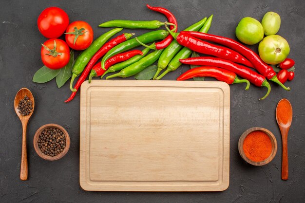 Vista dall'alto peperoni rossi e verdi piccanti e pomodori foglie di alloro ciotole di polvere di peperone rosso e pepe nero e un tagliere tra le ciotole a terra