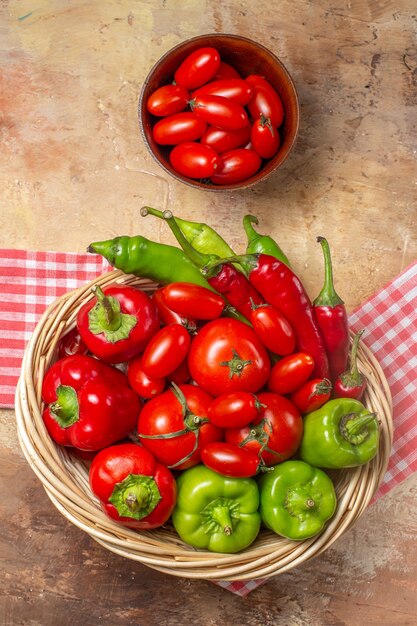 Vista dall'alto peperoni verdi e rossi peperoni piccanti pomodori in cesto di vimini pomodorini in ciotola asciugamano da cucina su sfondo ambrato