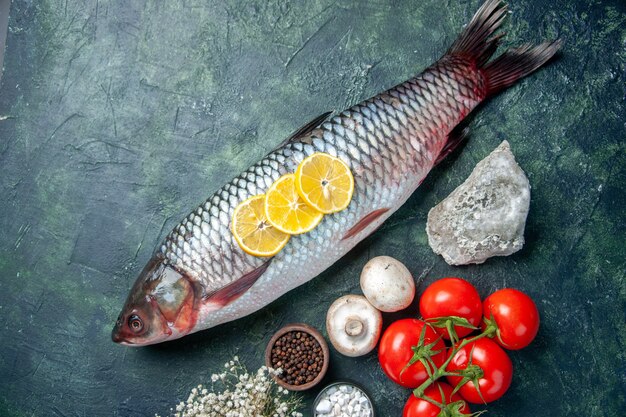 vista dall'alto pesce crudo fresco con pomodori e limone su sfondo blu scuro