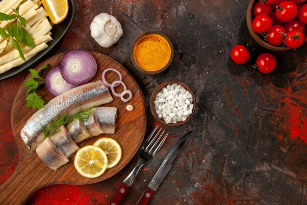 Vista dall'alto pesce fresco a fette con anelli di cipolla e pomodori freschi sullo sfondo scuro