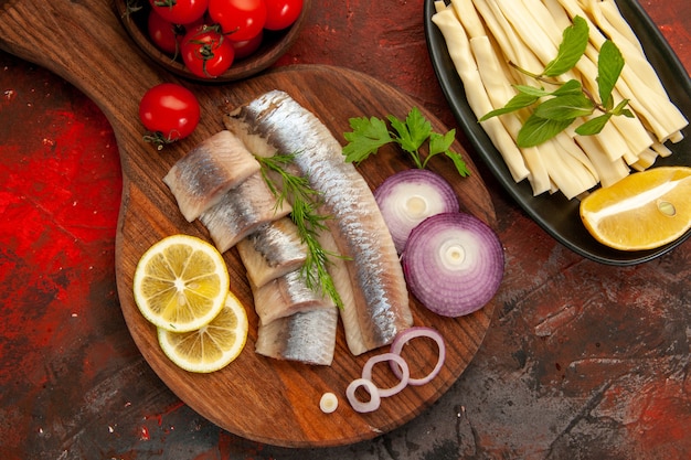 Vista dall'alto pesce fresco a fette con anelli di cipolla e pomodori freschi sullo sfondo scuro