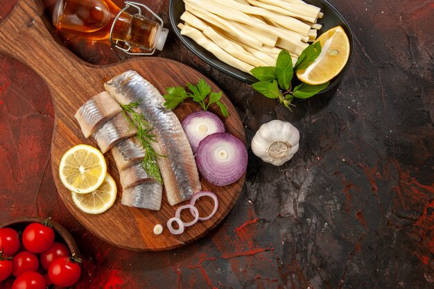 Vista dall'alto pesce fresco a fette con anelli di cipolla e pomodori su sfondo scuro