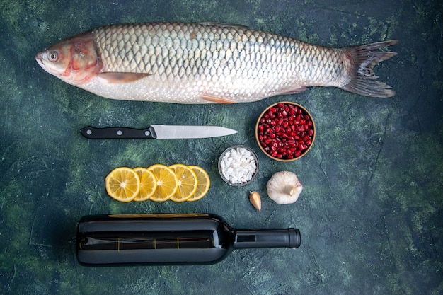 Vista dall'alto pesce fresco fette di limone coltello semi di melograno ciotola bottiglia di vino sul tavolo della cucina