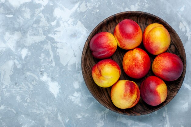 Vista dall'alto pesche fresche frutta pastosa e gustosa all'interno del piatto marrone sulla scrivania bianco chiaro