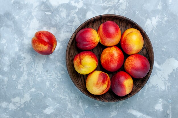 Vista dall'alto pesche fresche frutti morbidi e gustosi all'interno del piatto marrone sulla superficie bianca chiara