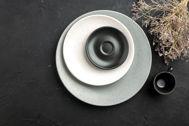 Vista dall'alto piattino nero e piatto bianco sulla piastra grigia ramo di fiori secchi tazza nera su spazio libero superficie scura