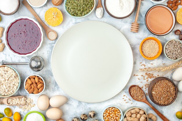 Vista dall'alto piatto bianco ciotole con mandorle semi di mais arachidi chicchi di grano semi di sesamo uova miele bastoncini uova di quaglia