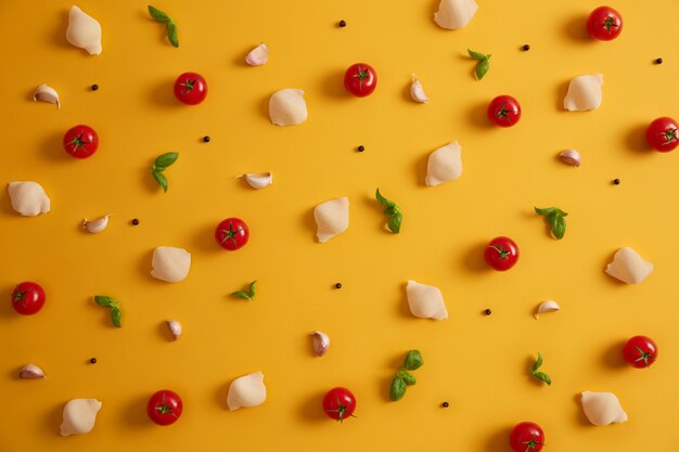 Vista dall'alto piatto di gusci di pasta di grano duro, pomodorini rossi, basilico e aglio per preparare il piatto italiano. Verdure e spezie su sfondo giallo. Ingredienti da cucina. Cibo disintossicante