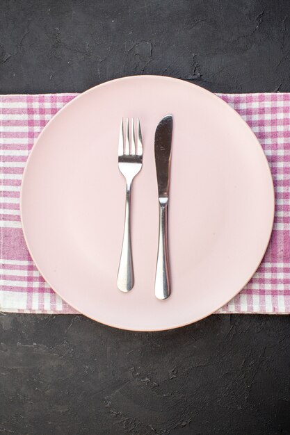 Vista dall'alto piatto rosa con forchetta e coltello su sfondo scuro