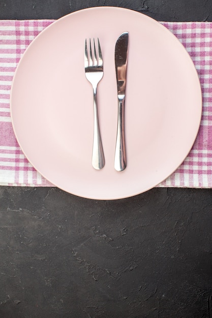 Vista dall'alto piatto rosa con forchetta e coltello su sfondo scuro