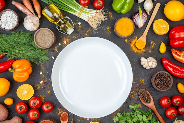 Vista dall'alto piatto rotondo bianco pepe nero curcuma e sale marino in piccole ciotole aglio pomodori coriandolo aneto cipolle verdi bottiglia di olio sul tavolo