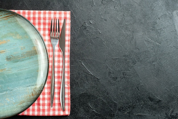 Vista dall'alto piatto rotondo cena coltello e forchetta sul tovagliolo a quadretti rosso e bianco sulla tavola nera con spazio libero