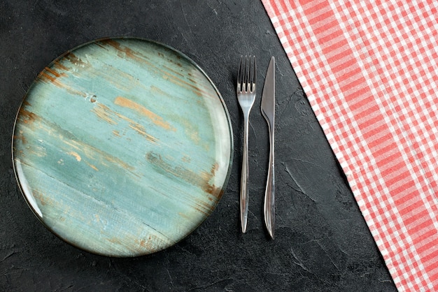 Vista dall'alto piatto rotondo forchetta e coltello da cena tovaglia a quadretti rossa e bianca sulla tavola nera