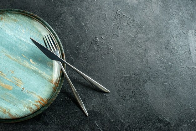 Vista dall'alto piatto rotondo in acciaio forchetta e coltello da cena sulla tavola nera con spazio libero