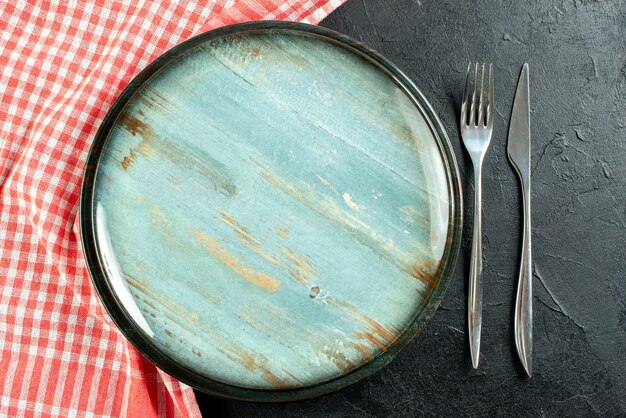 Vista dall'alto piatto rotondo in acciaio forchetta e coltello da cena tovaglia a quadretti rossa e bianca sulla tavola nera