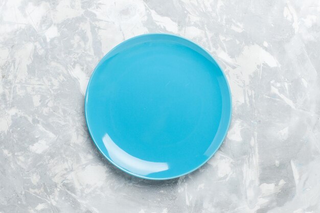 Vista dall'alto piatto rotondo vuoto blu ed su superficie bianca