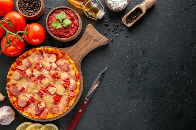 Vista dall'alto piccola deliziosa pizza con pomodori rossi freschi sullo spazio libero per la consegna del tavolo scuro