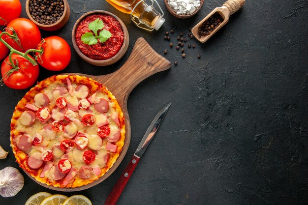 Vista dall'alto piccola deliziosa pizza con pomodori rossi freschi sullo spazio libero per la consegna del tavolo scuro