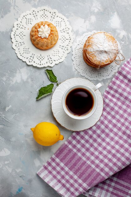 Vista dall'alto piccola deliziosa torta con tè e limone acido sul colore del biscotto dolce del biscotto della torta della scrivania leggera