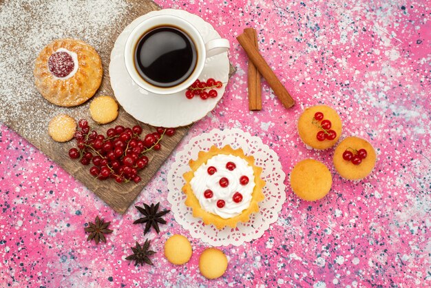 Vista dall'alto piccola torta con biscotti alla crema mirtilli rossi freschi insieme a una tazza di caffè e cannella sul biscotto di superficie colorata