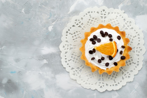 Vista dall'alto piccola torta con fetta d'arancia e crema sul dolce scrivania grigio