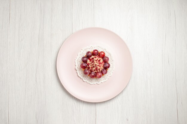 Vista dall'alto piccola torta con l'uva all'interno del piatto sul tavolo bianco, torta di frutta dolce