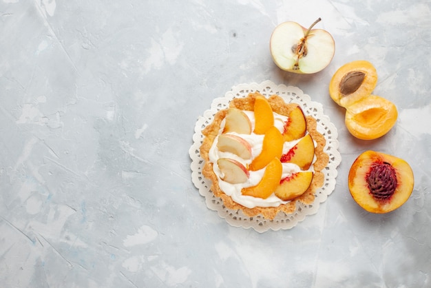 Vista dall'alto piccola torta cremosa con frutta a fette e crema bianca sul pavimento luce bianca torta di frutta biscotto dolce cuocere