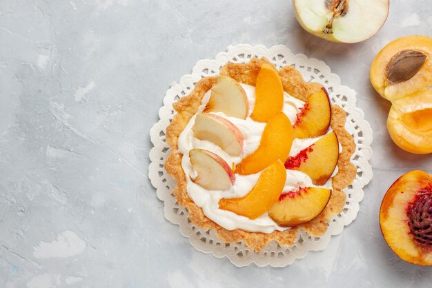 Vista dall'alto piccola torta cremosa con frutta a fette e crema bianca sulla scrivania a luce bianca torta di frutta dolcezza biscotto biscotto cuocere