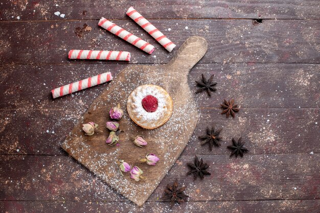 Vista dall'alto piccola torta cremosa con lampone insieme a caramelle rosa stick sullo sfondo di legno marrone caramelle dolci zucchero cuocere la torta