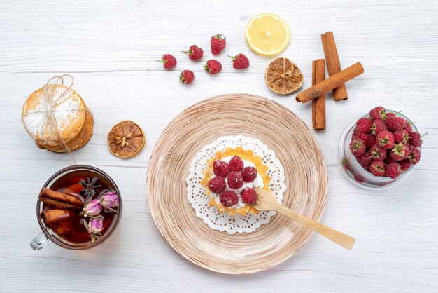 Vista dall'alto piccola torta deliziosa con panna e lamponi insieme a biscotti sandwich tè alla cannella sul tavolo bianco chiaro frutta bacca torta biscotto dolce