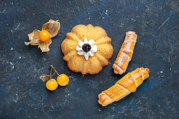 Vista dall'alto piccola torta deliziosa insieme a braccialetti dolci sulla frutta dolce torta biscotto scuro scrivania