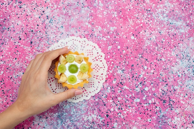 Vista dall'alto piccola torta gustosa con kiwi a fette di crema e banane sul biscotto dolce zucchero torta viola scrivania