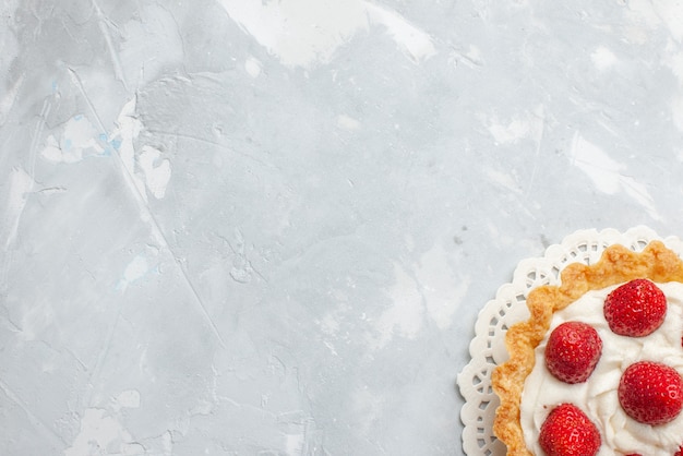 Vista dall'alto piccola torta gustosa con panna e fragole rosse fresche sulla crema dolce del biscotto di bacca di frutta torta leggera da scrivania