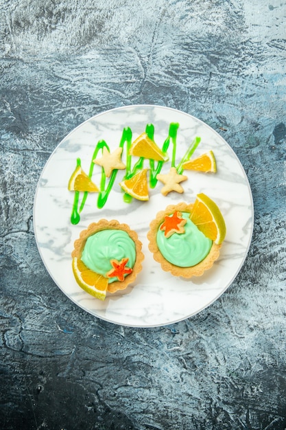 Vista dall'alto piccole crostate con crema pasticcera verde e fetta di limone sul piatto sul posto libero tavolo scuro
