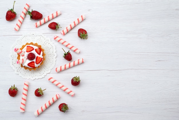 Vista dall'alto piccole deliziose torte con crema e fragole a fette caramelle sullo sfondo bianco torta bacca dolce cuocere