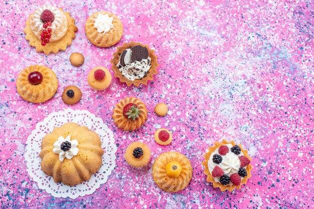 Vista dall'alto piccole deliziose torte con crema insieme a diversi frutti di bosco sullo sfondo luminoso torta biscotto bacca dolce cuocere