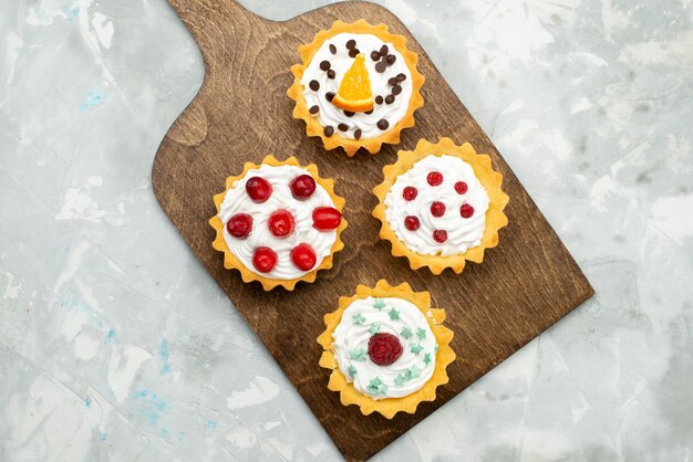 Vista dall'alto piccole torte alla crema con frutta sulla superficie grigio chiaro zucchero dolce