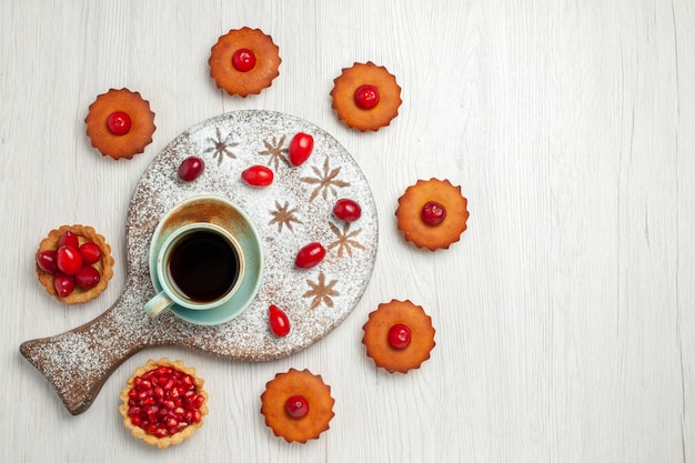 Vista dall'alto piccole torte con frutta e tazza di tè sullo scrittorio bianco chiaro