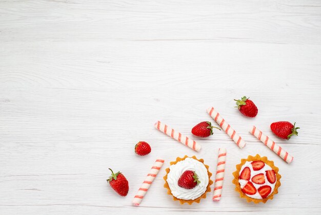 Vista dall'alto piccole torte cremose con fragole fresche e caramelle sullo sfondo chiaro torta dolce foto frutti di bosco cuocere