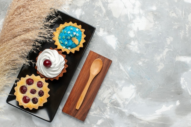 Vista dall'alto piccole torte cremose con panna e frutta sulla crema di biscotti dolci torta sfondo chiaro